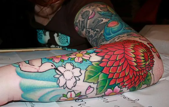 Colorful Zinnia flower with bird tattoo on arm