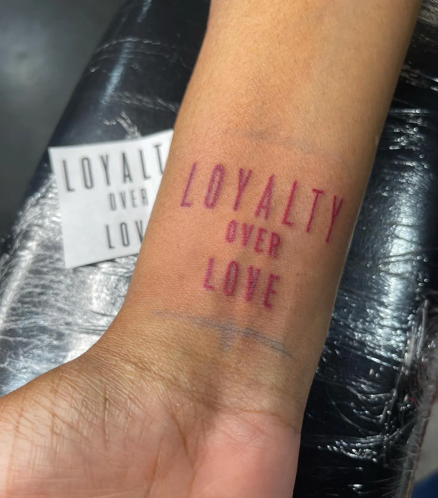 Loyalty Over Love in Red Ink on Forearm