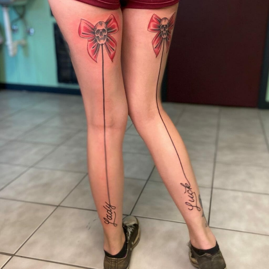 Bow Design And Skull Ribbon Tattoo On Back Of Thigh