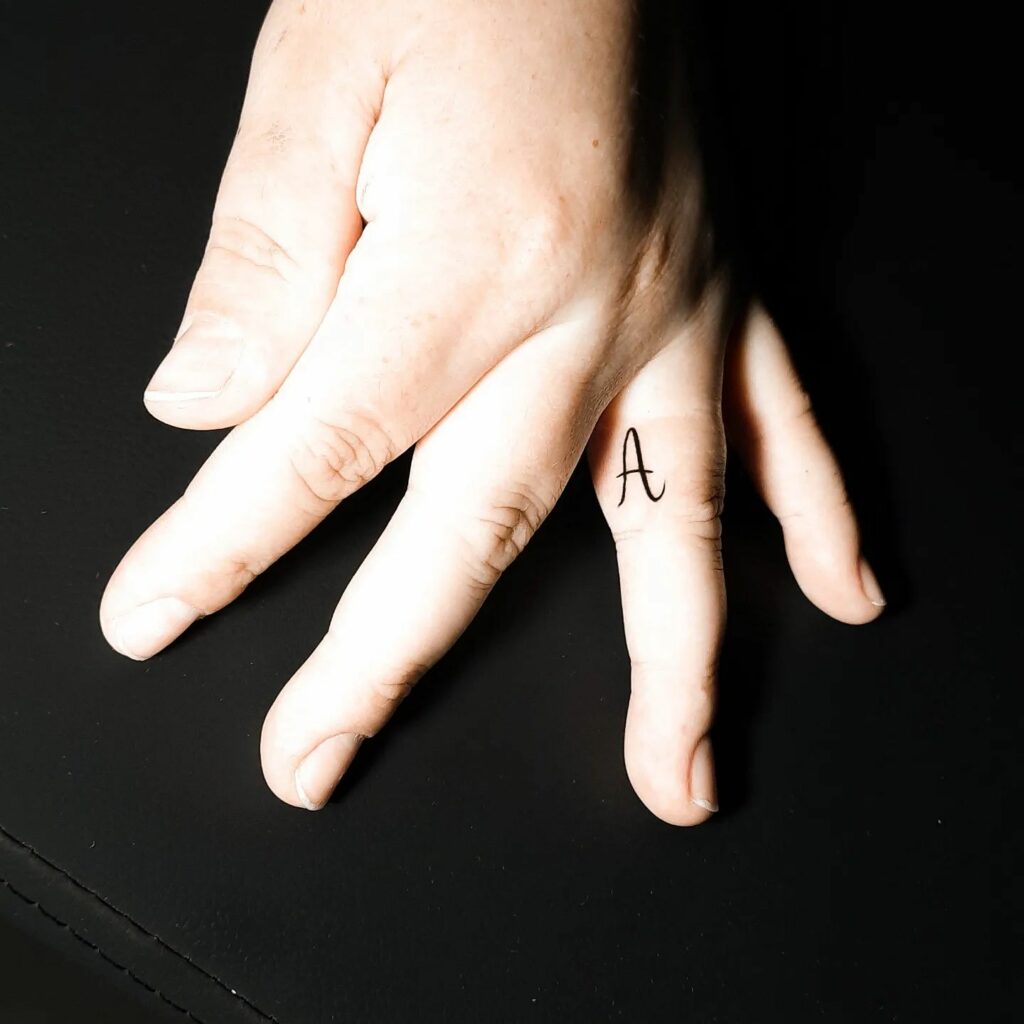 Tatouage initial minimaliste sur le doigt intérieur