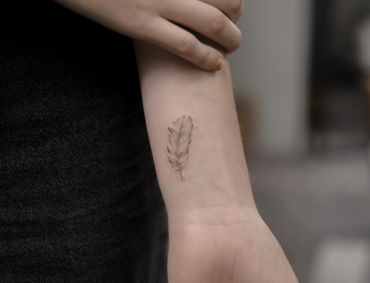 Tiny black hand feather tattoo